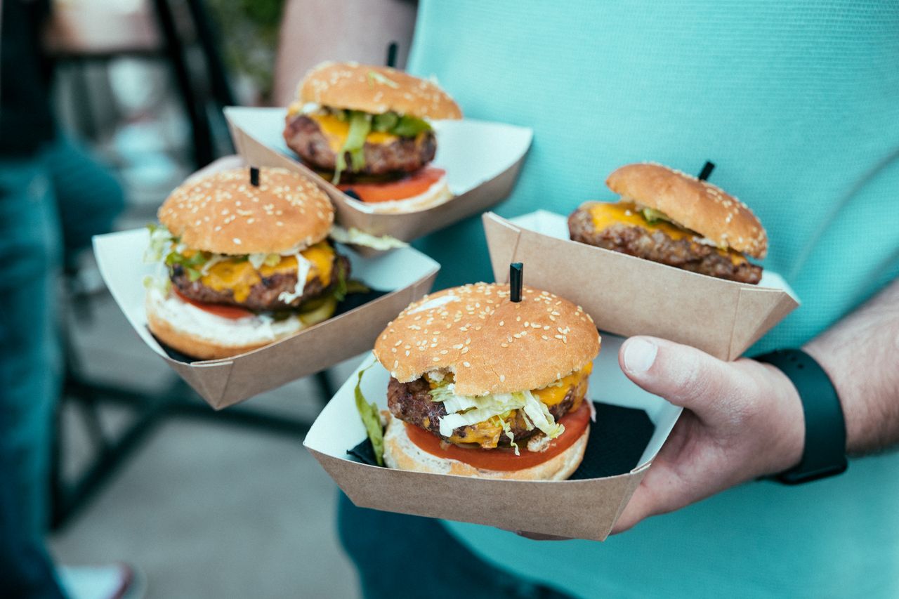 A close-up of hands holding four juicy beef burgers in cardboard trays, ideal for food lovers.